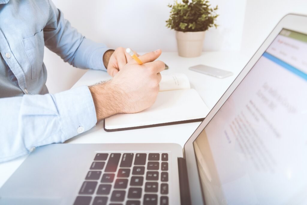 person holding pencil near laptop computer